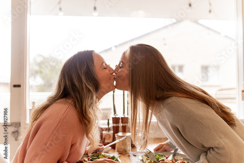 Female same sex couple kissing across the dining table at home