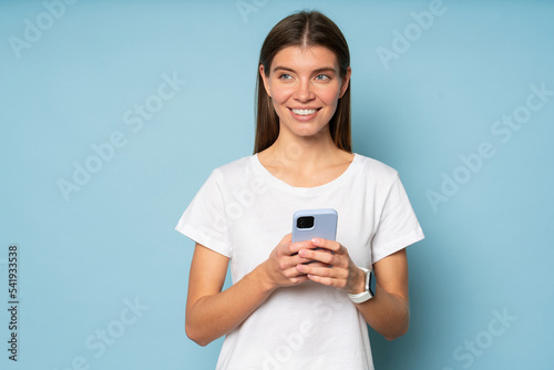 Woman using phone on blue background looking aside thinking over her respond in online chat