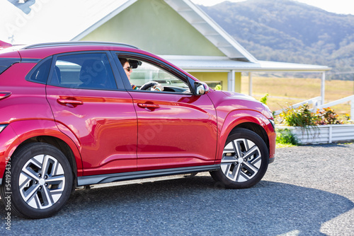 Driving red electric vehicle past country farm house on hilltop