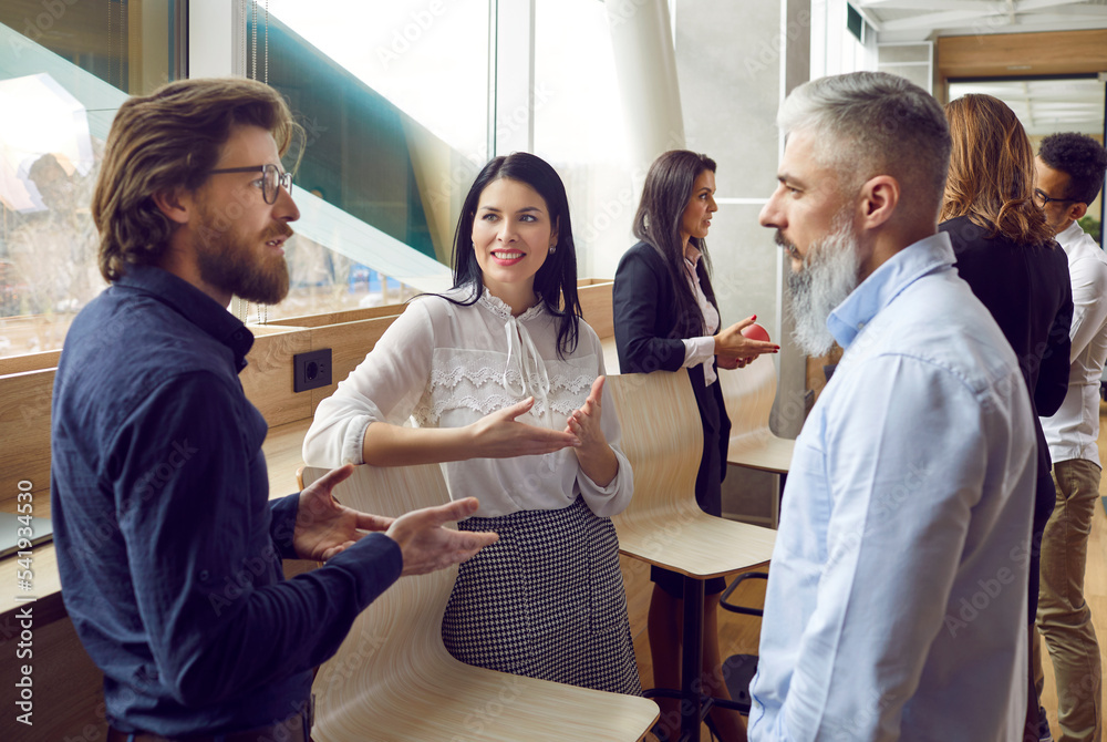 Different people communicating at a business meeting. Group of men and women standing by an office window, talking, discussing work and sharing opinions on business management. Communication concept Different people communicating at a business meeting. Group of men and women standing by an office window, talking, discussing work and sharing opinions on business management. Communication concept