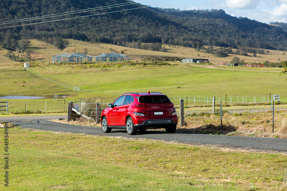 Red electric vehicle car driving down rural country road on sunlit day Red electric vehicle car driving down rural country road on sunlit day