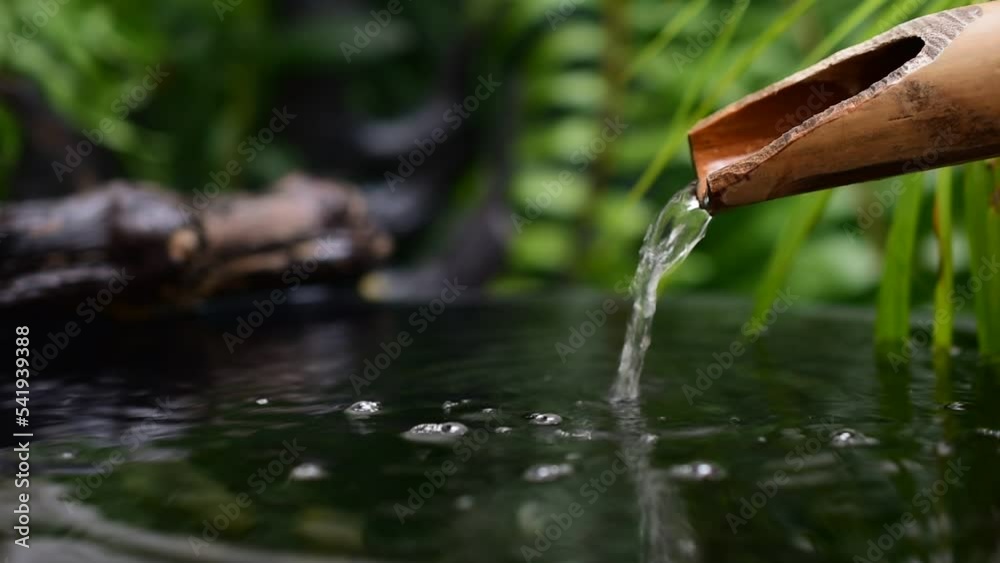 Water flows from bamboo gutter pipes with smoke floating on abstract pattern wall background.
