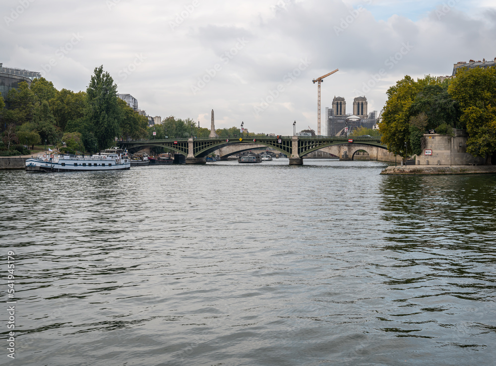 Fototapeta premium Looking West on the River Seine with the Pont Sully and scaffolding shrouded Notre Dame in the distance, Paris, France, repairs, church, cathedral, scaffolding, crane, towers, sully, bridge, pont sull