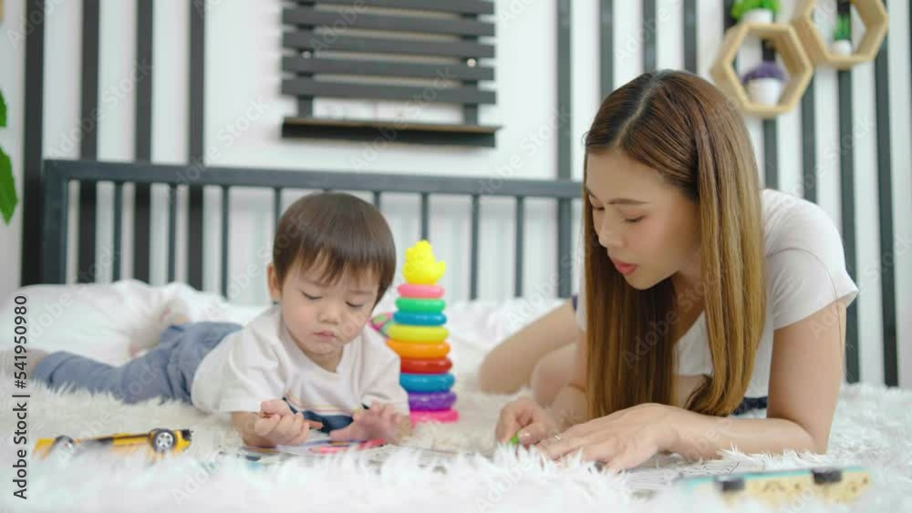 Happy asian little son painting with crayon and colored pencil with his mother in bedroom at home. Mom teaching son how to painting with crayon color on book or doing homework. family psychology Happy asian little son painting with crayon and colored pencil with his mother in bedroom at home. Mom teaching son how to painting with crayon color on book or doing homework. family psychology