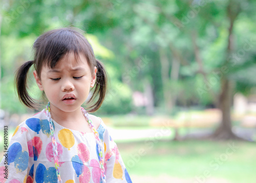 Headshot of sad 4 years old cute baby Asian girl, little toddler child with adorable pigtails hair making frustrated face, looking down with copy space background.