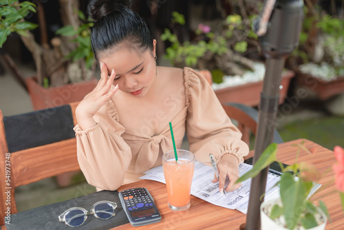 A young female entrepreneur is pressured with the calculations and filling of forms as she dines in an al fresco restaurant with a cold beverage.