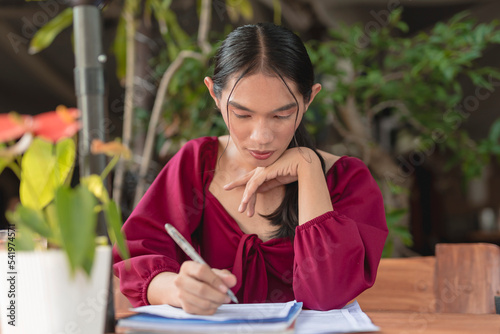 A hardworking transgender woman prepares for her exam as she studies her reading materials at an outdoor cafe.