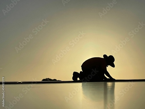 Silhouette of a man down on his knees while wearing a fedora hat before the beige background