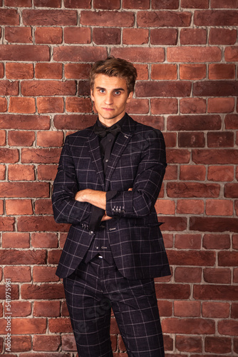 Confident young businessman entrepreneur looking at camera at brick wall background. Caucasian male adult in studio. Stylish handsome man model in suit indoors. Fashion style concept. Copy space