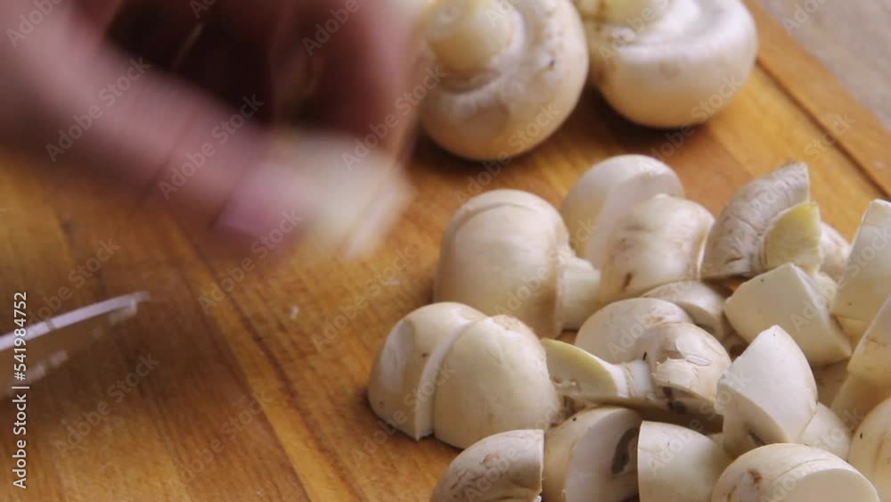 A bunch of chopped champignon mushrooms on the kitchen table, the hand of the cook with a kitchen knife. A bunch of chopped champignon mushrooms on the kitchen table, the hand of the cook with a kitchen knife.