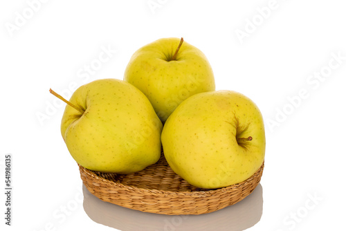 Three ripe yellow apples on a straw plate, macro, isolated on white background.