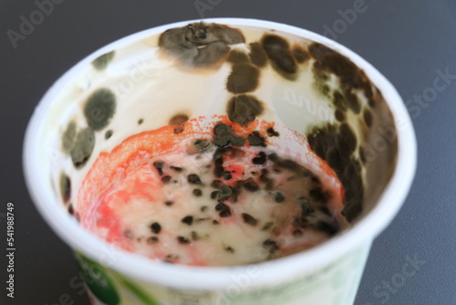 sour cream in a plastic container covered with pink and grey mold