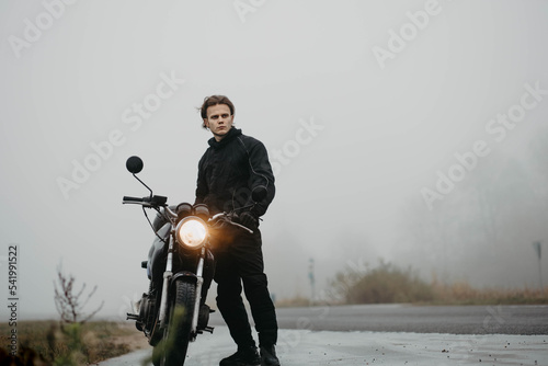 Fotografiet male motorcyclist on the road with a motorcycle in the rain in cold weather, tra