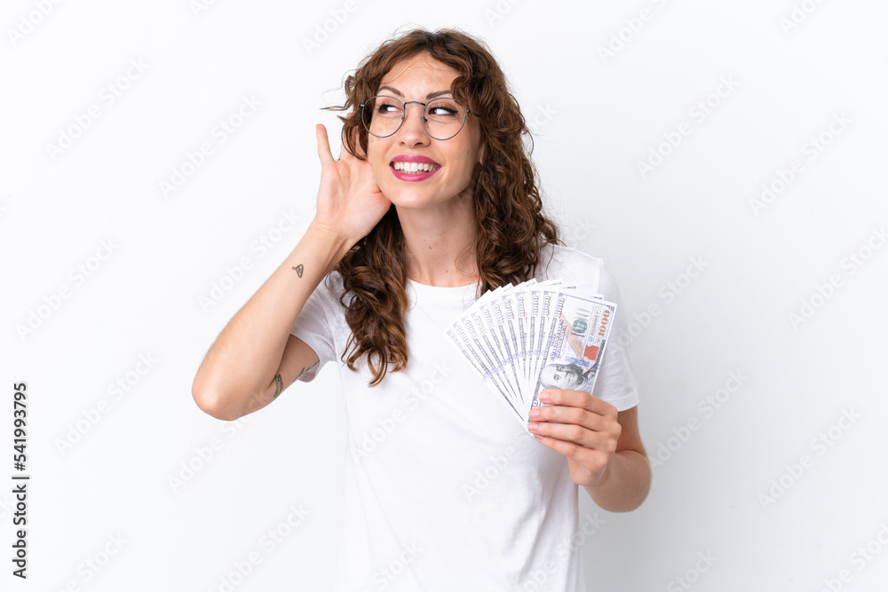 Young woman with curly hair taking a lot of money isolated background on white background listening to something by putting hand on the ear Young woman with curly hair taking a lot of money isolated background on white background listening to something by putting hand on the ear