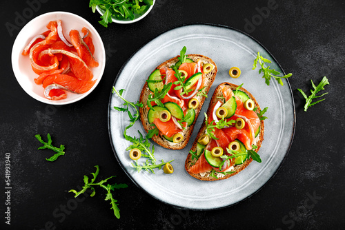 Toasts with salted salmon, arugula, green olives and cucumber. Top view