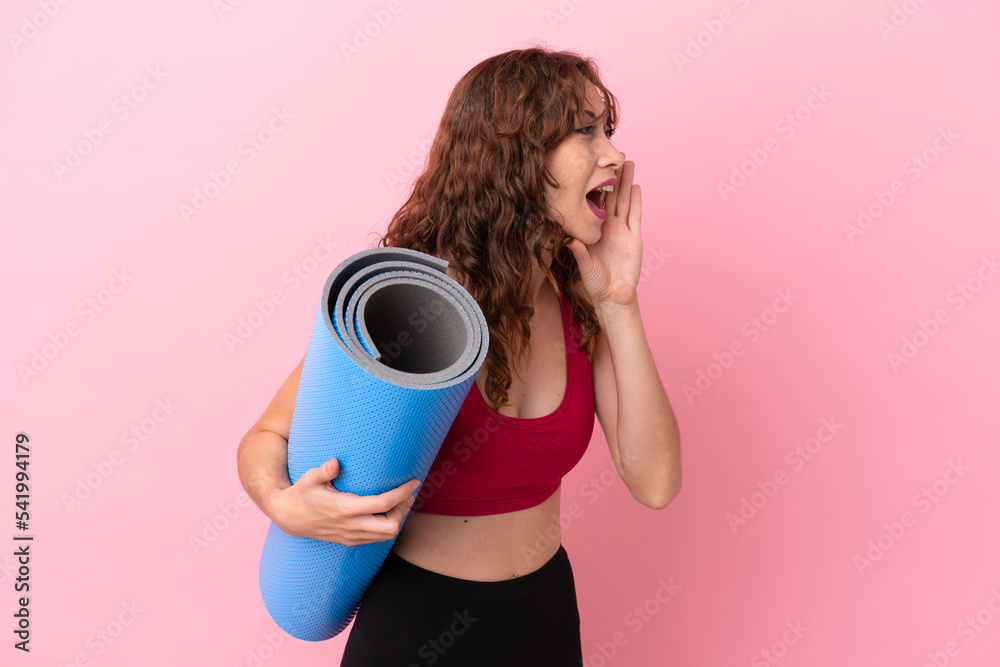 Obraz premium Young sport woman going to yoga classes while holding a mat isolated on pink background shouting with mouth wide open to the side