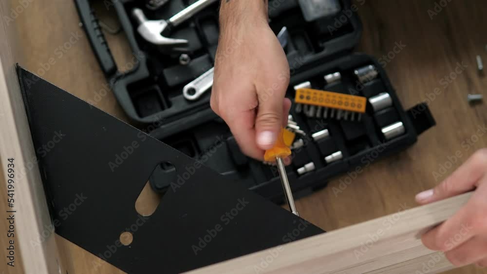 Close-up of a man's hands assembling a wooden bed using a screwdriver to insert screws into the bed frame.Collection of wooden furniture.Husband for an hour. Self-assembly using a guide. House design. Close-up of a man's hands assembling a wooden bed using a screwdriver to insert screws into the bed frame.Collection of wooden furniture.Husband for an hour. Self-assembly using a guide. House design.