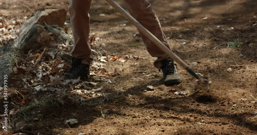 Trailer worker rakes leaves and branches from nature trail in autum - slow motion side profile