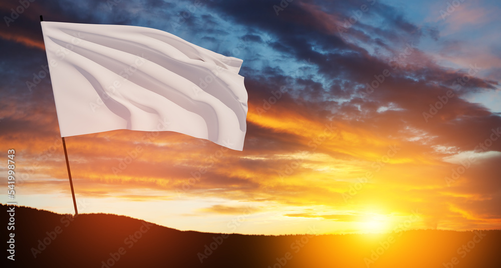 White flag waving in the wind on flagpole against the sunset sky with ...