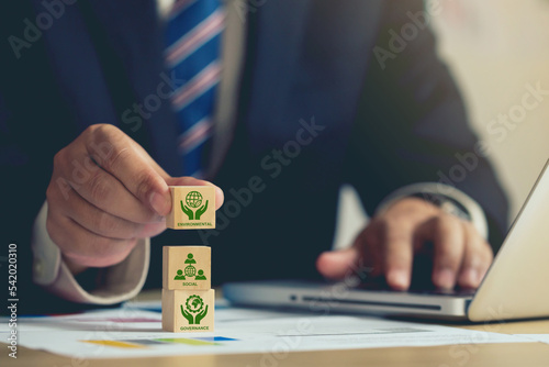 Obraz na płótnie ESG concept of environmental, Businessman hand holding wooden cube block with ESG icon with copy space, Businessman Planing an ESG Project on laptop