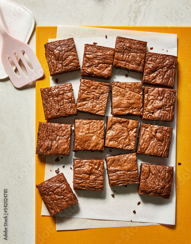 Homemade cut brownies on an orange cutting board with spatula