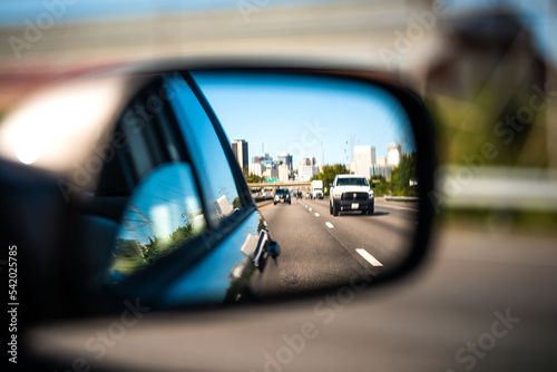 Car window side mirror on sunny day with truck traffic in reflection in Richmond, Virginia transportation highway street road