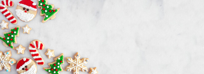 Cute Christmas cookie corner border. Top down view on a white marble banner background with copy space. Holiday baking concept. Santa Claus, tree, snowflakes, candy canes, stars.