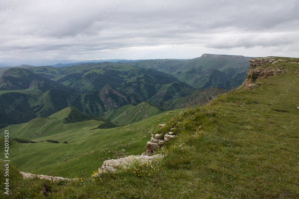 Panoramic view of green mountains and hills from the Bermamyt plateau in Karachay-Cherkessia in Russia on a cloudy summer day and copy space in a hazy haze on the horizon