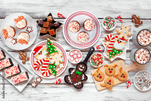 Cute Christmas sweets and cookie table scene. Top view over a rustic white wood background. Fun holiday baking concept.