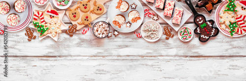 Cute Christmas sweets and cookie top border. Above view over a rustic white wood banner background with copy space. Fun holiday baking concept.