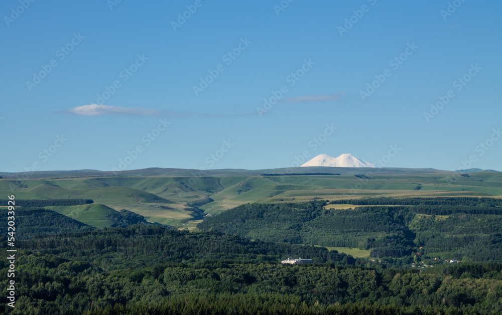 Panoramic view of the green valley and the snowy peak of Mount Elbrus on the horizon against the blue sky on a sunny clear morning in Kislovodsk Stavropol territory russia and the space for copying