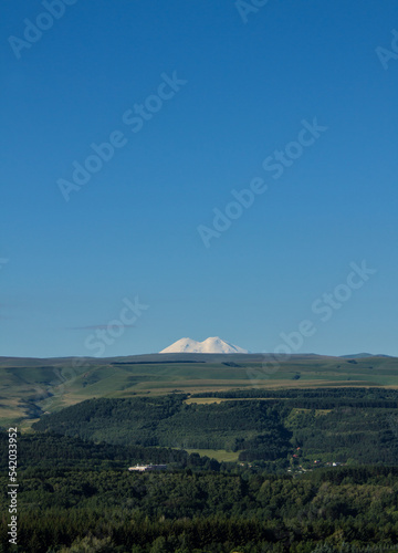 Panoramic view of the green valley and the snowy peak of Mount Elbrus on the horizon against the blue sky on a sunny clear morning in Kislovodsk Stavropol territory russia and the space for copying