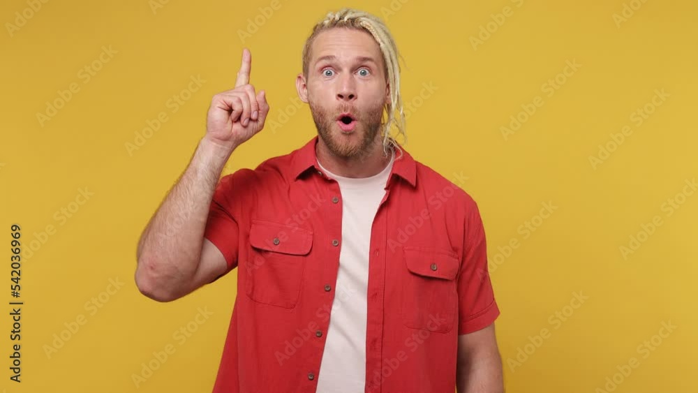Young insighted smart blond man with dreadlocks 30s wear red shirt white t-shirt looks around thinks scratches at temple comes up with ideas raised finger get plan isolated on plain yellow background Young insighted smart blond man with dreadlocks 30s wear red shirt white t-shirt looks around thinks scratches at temple comes up with ideas raised finger get plan isolated on plain yellow background