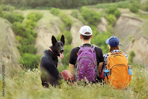 Back view of a sitting at the hill hiking couple with a dog