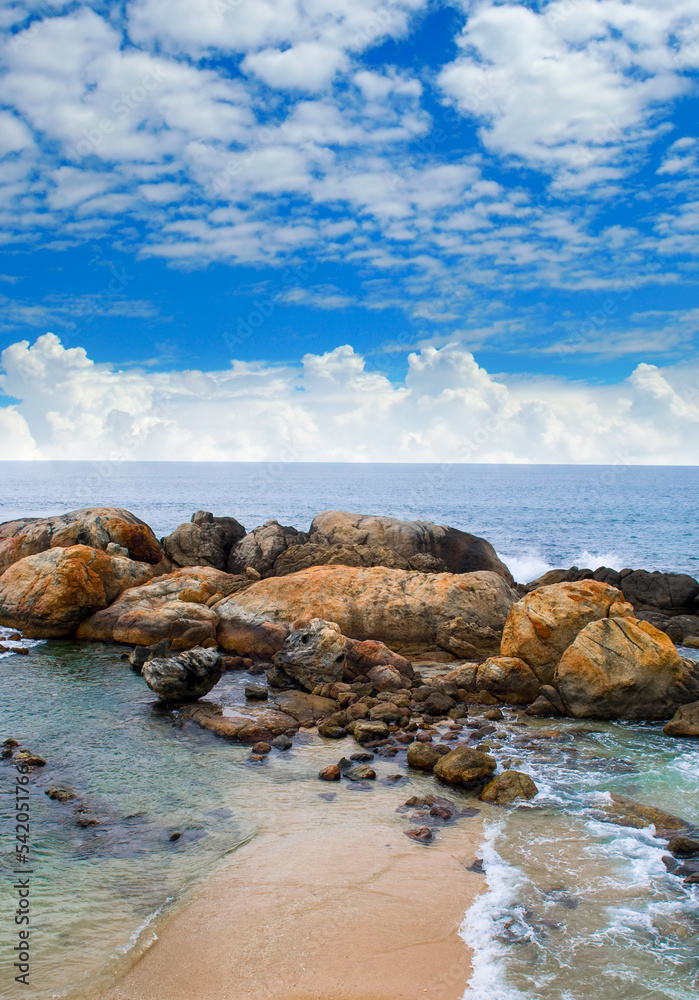 Stony sea beach, blue tropical ocean and beautiful cloudy sky. Vertical photo.