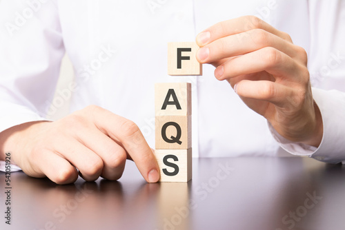 wooden cubes with the word FAQS, the hand puts a cube with letter F.