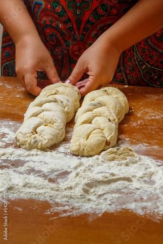 The hands of a Jewish woman weave challah with a pigtail for Shabbat.
