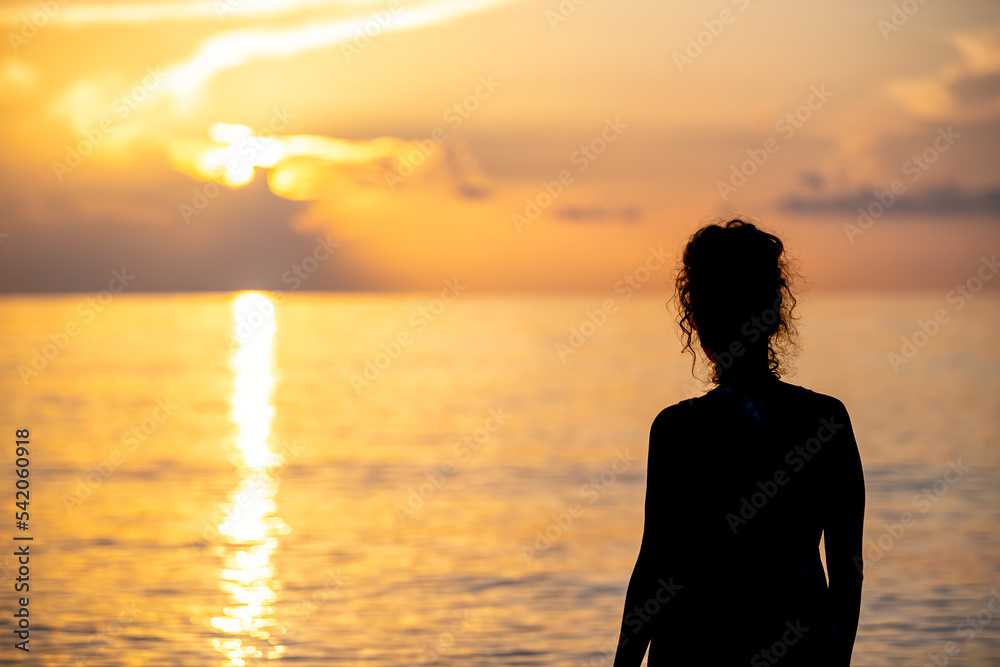 Hollywood Beach in Miami, Florida morning sunrise sun behind sky clouds with reflection path, woman watching looking at calm still landscape