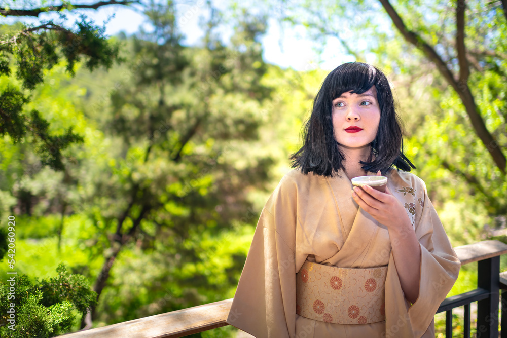 Portrait of young caucasian girl woman happy face smiling, drinking cup of green tea outside in outdoor backyard garden with black hair Portrait of young caucasian girl woman happy face smiling, drinking cup of green tea outside in outdoor backyard garden with black hair
