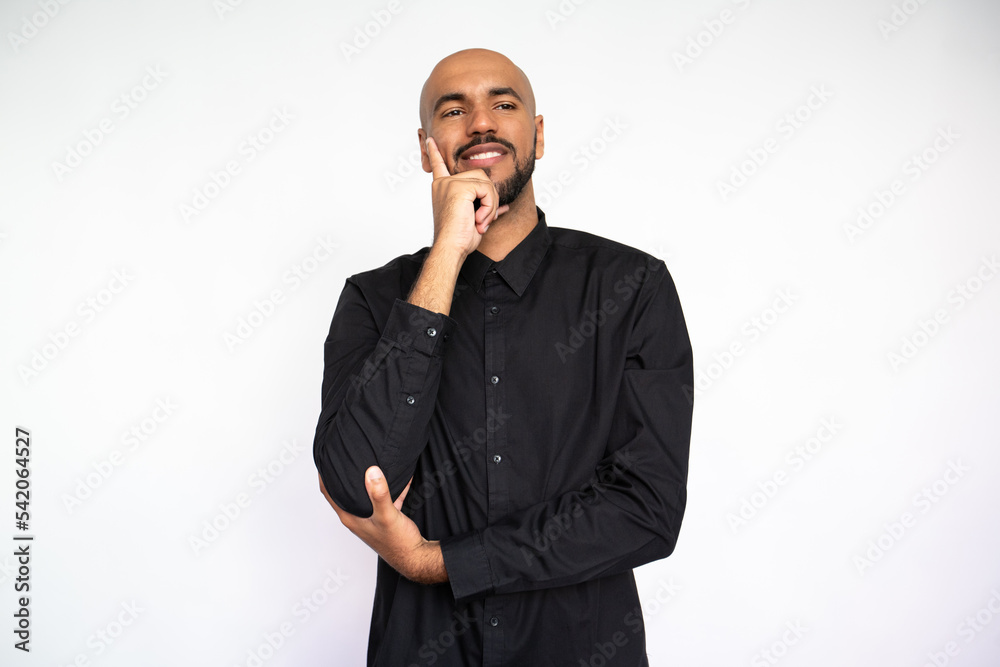 Portrait of pensive young man leaning on hand. Happy Latin American male model with bald head and beard in black shirt looking away, smiling and touching cheek. Contemplation, focus concept Portrait of pensive young man leaning on hand. Happy Latin American male model with bald head and beard in black shirt looking away, smiling and touching cheek. Contemplation, focus concept