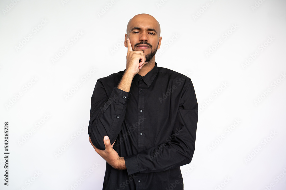 Portrait of focused young man leaning on hand. Serious Latin American male model with bald head and beard in black shirt looking at camera, touching cheek. Contemplation, focus concept Portrait of focused young man leaning on hand. Serious Latin American male model with bald head and beard in black shirt looking at camera, touching cheek. Contemplation, focus concept