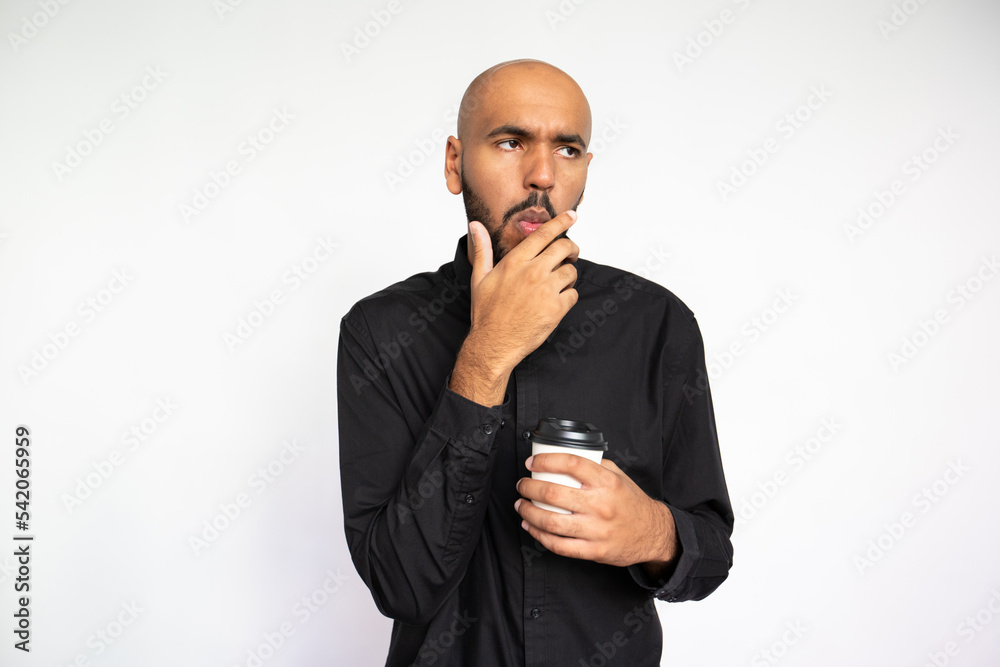 Portrait of impressed young man with coffee. Thoughtful African American male model with bald head in black shirt looking away, touching chin. Coffee break, approval concept Portrait of impressed young man with coffee. Thoughtful African American male model with bald head in black shirt looking away, touching chin. Coffee break, approval concept