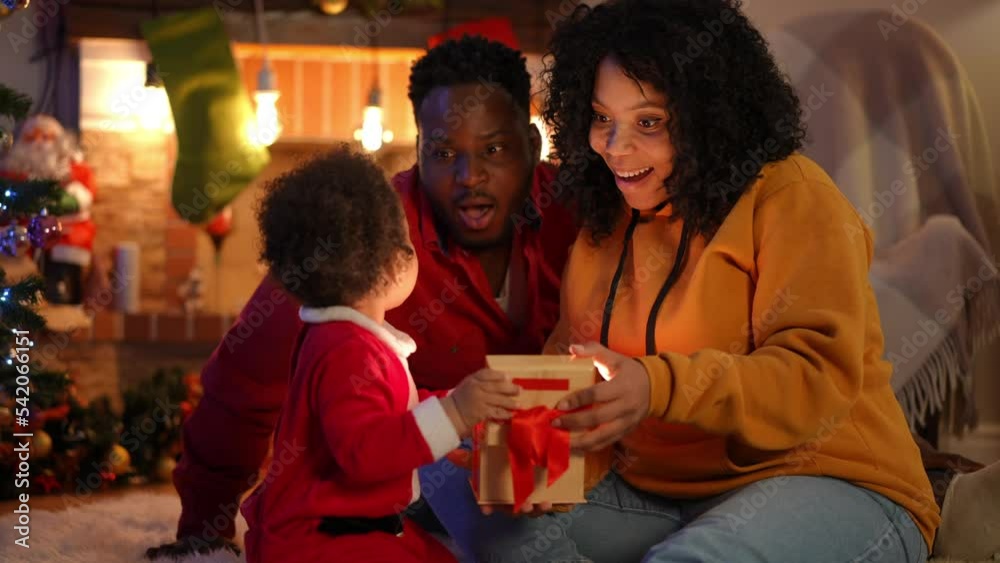 Curios little boy man and woman opening Christmas gift box with light inside with surprised facial expression. Happy relaxed positive African American young family celebrating New Year at home Curios little boy man and woman opening Christmas gift box with light inside with surprised facial expression. Happy relaxed positive African American young family celebrating New Year at home