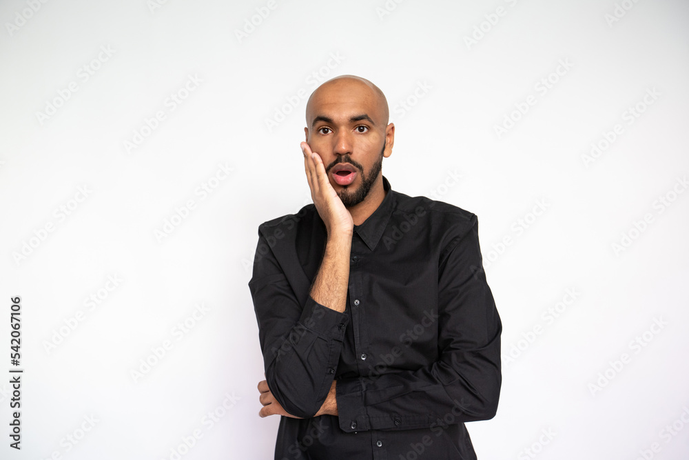 Portrait of astonished young man looking at camera. Bearded businessman wearing black shirt standing with open mouth with surprised expression. Surprise concept Portrait of astonished young man looking at camera. Bearded businessman wearing black shirt standing with open mouth with surprised expression. Surprise concept