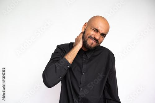 Portrait of frowning young businessman rubbing neck against white background. Tired bearded man wearing black shirt having neck pain. Muscle pain concept photo