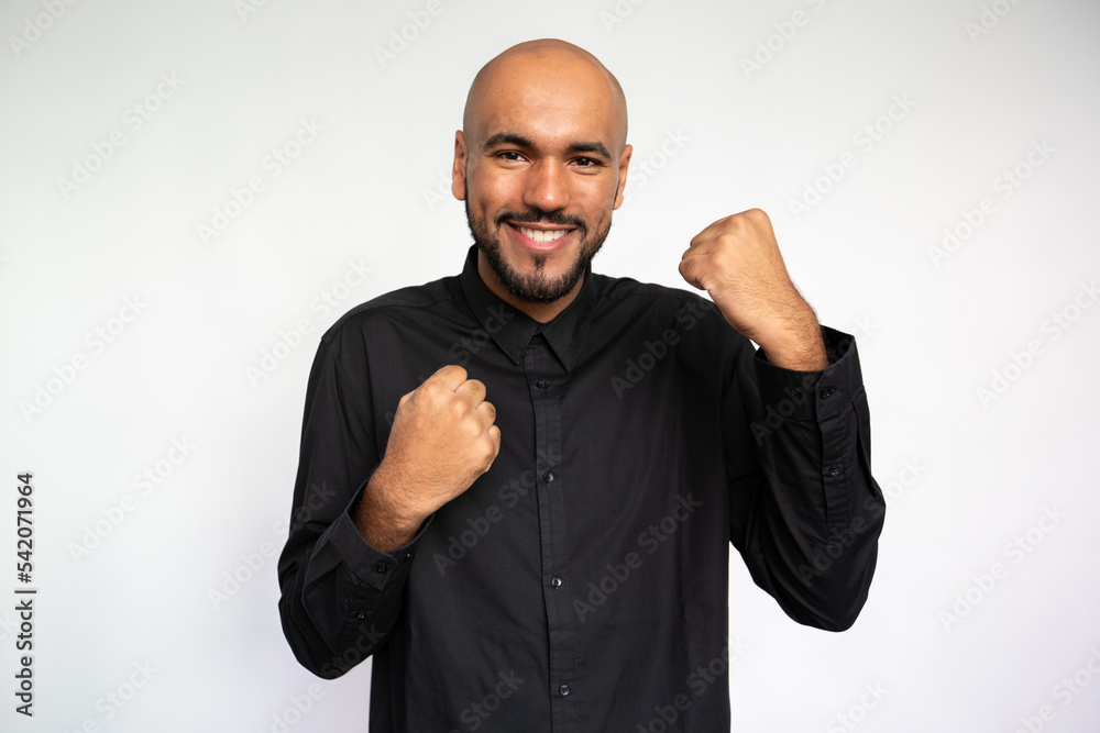 Portrait of happy young man with clenched fists. Joyful multiethnic male model with bald head in black shirt looking at camera, making winner gesture and celebrating success. Achievement concept Portrait of happy young man with clenched fists. Joyful multiethnic male model with bald head in black shirt looking at camera, making winner gesture and celebrating success. Achievement concept