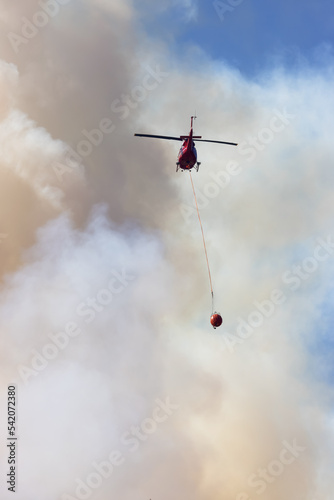 Wildfire Service Helicopter flying over BC Forest Fire and Smoke on the mountain near Hope during a hot sunny summer day. British Columbia, Canada. Natural Disaster