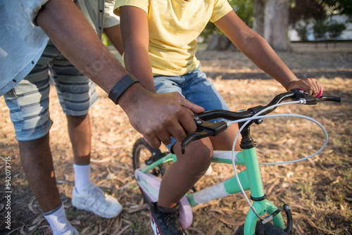 Close-up of African American mans and boys hands on bike handlebar. Careful dad holding little boy hand on small bike standing by his side both wearing casual clothes. Leisure, fatherhood concept