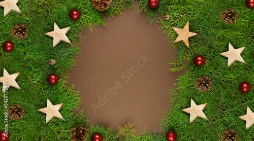 Christmas card on brown background with Thuja branches, red balls, wooden stars and place for text.
