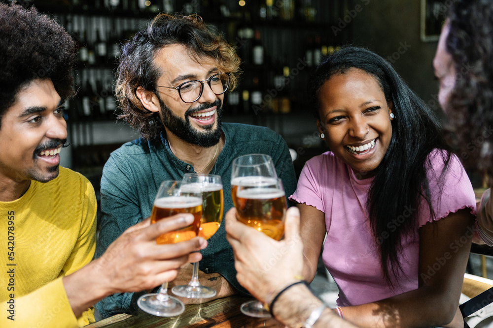 Group of diverse friends enjoying weekend together cheering with beers at brewery bar - International friendship concept